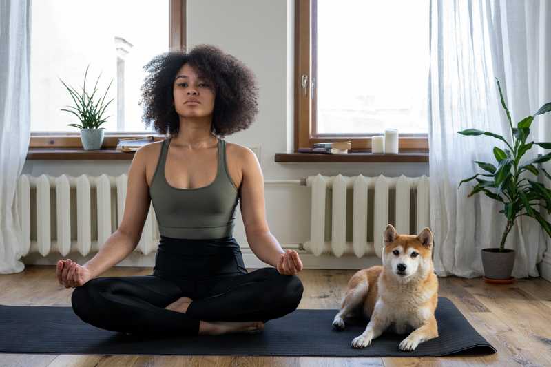 Woman sits next to her dog on a yoga mat 