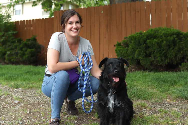 Brunette woman poses next to black dog in grass